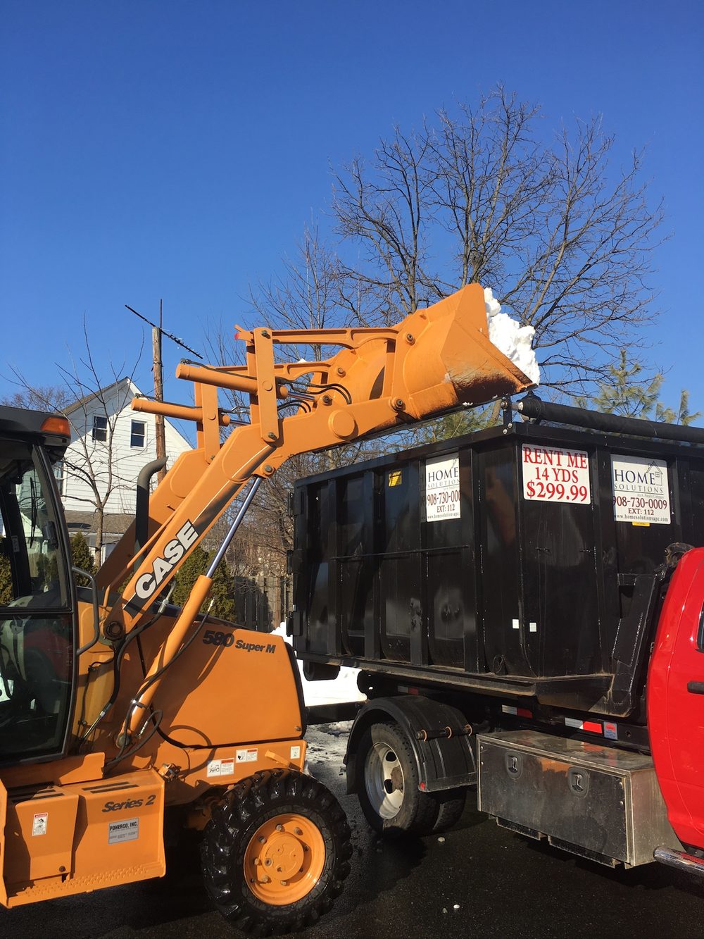 Backhoe loading plowed snow into a dumpster for off-site snow removal at a NJ commercial property