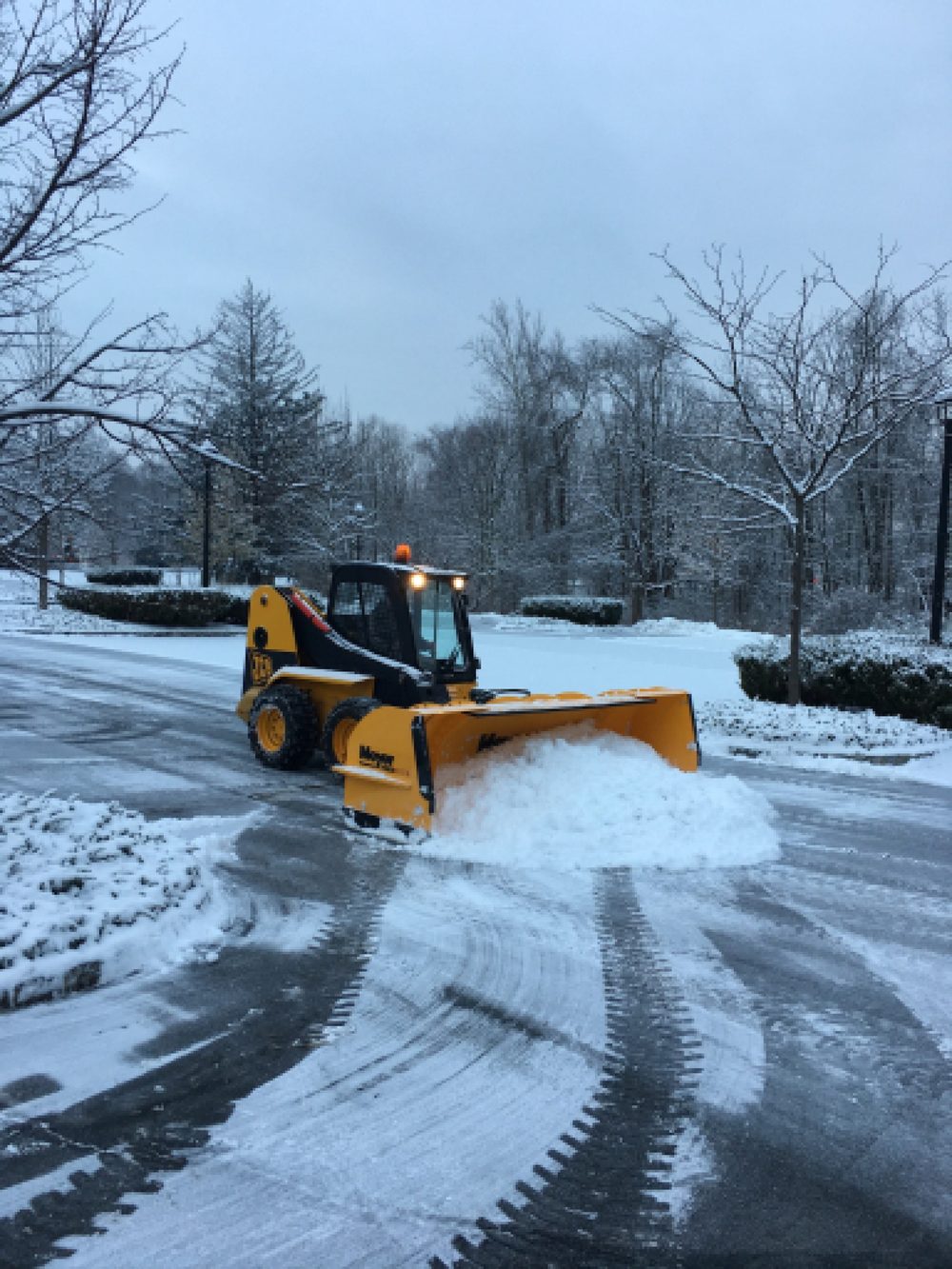 Skid steer with a snow pusher box clearing snow from a commercial parking lot in NJ